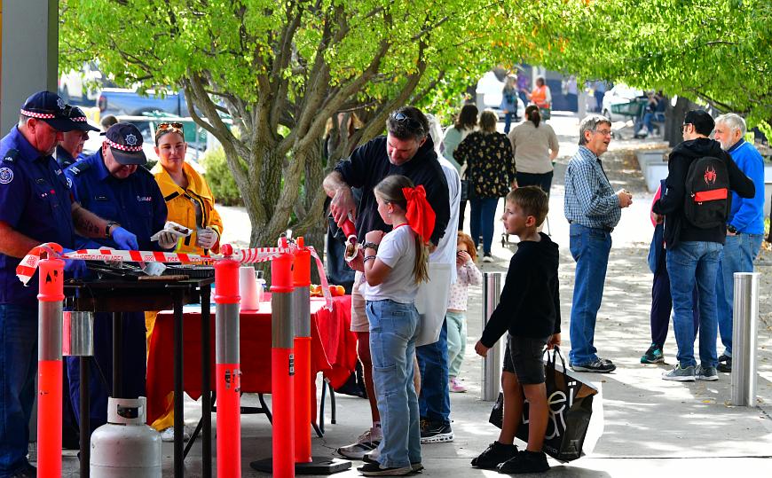 People lining up for CFA barbecue and people talking under trees
